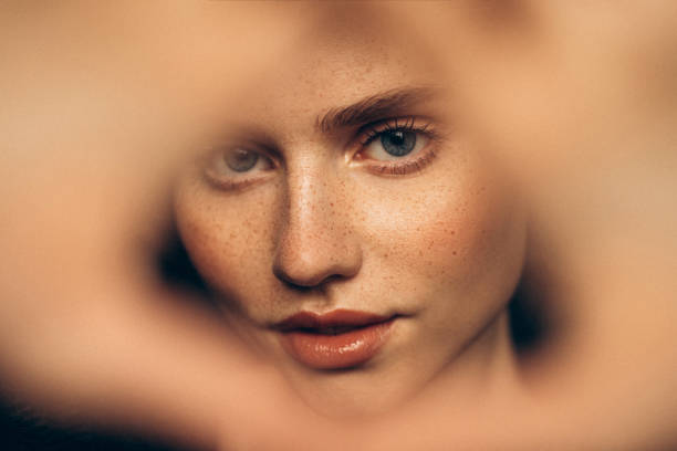 Gros plan sur un visage féminin avec des taches de rousseur, encadré de flou.