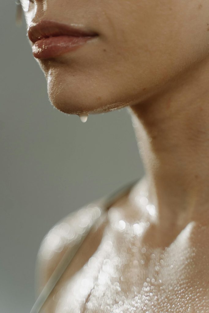 Détail sur la bouche et la clavicule, avec une goutte d'eau s'écoulant du menton et de l'eau sur le corps.